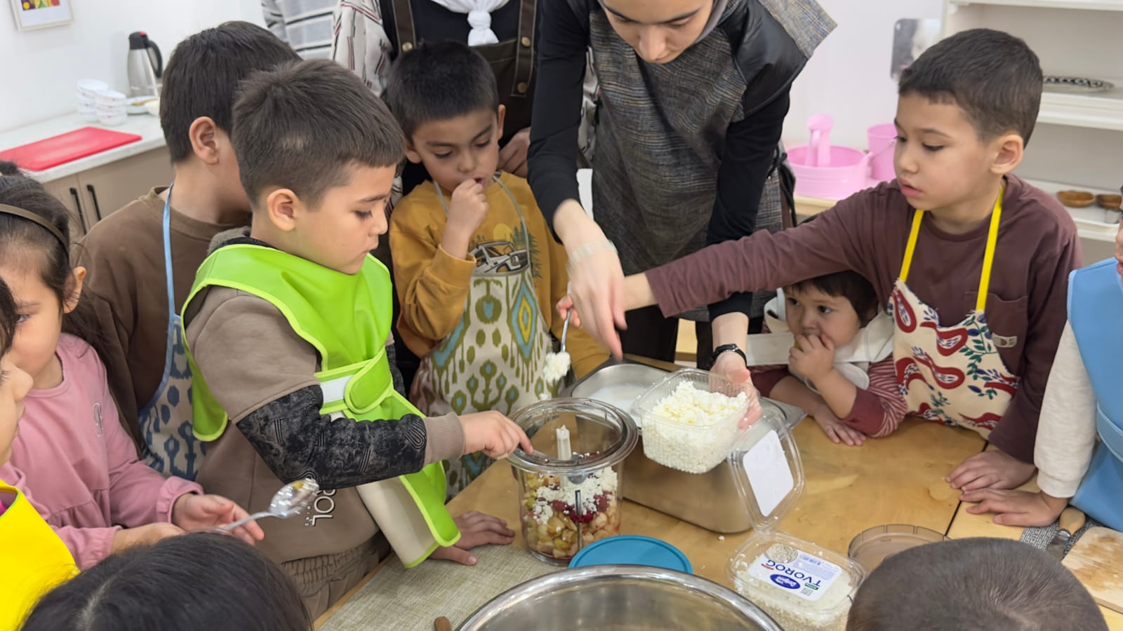 Fartuk kiyib murabbiy bilan birga ovqat tayyorlayotgan bolalar