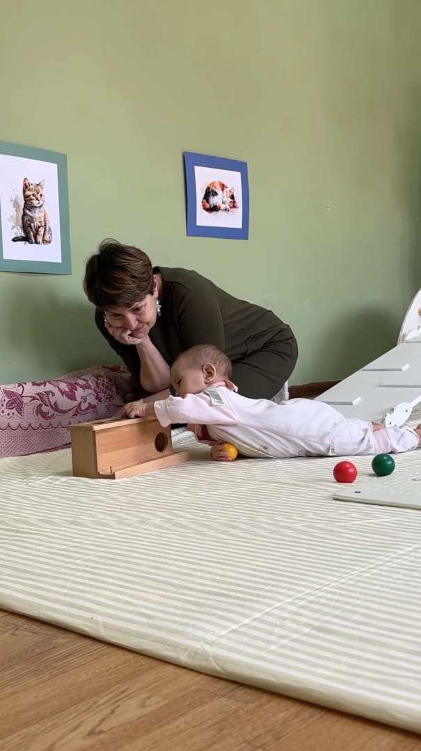 Qorni bilan yotib Montessori materialiga qo'l cho'zayotgan chaqaloq