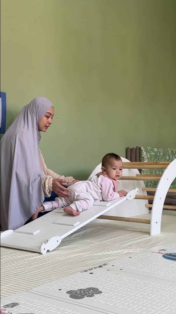 Chaqaloq Pikler qiyaligida yotganda yonida turgan ota-ona